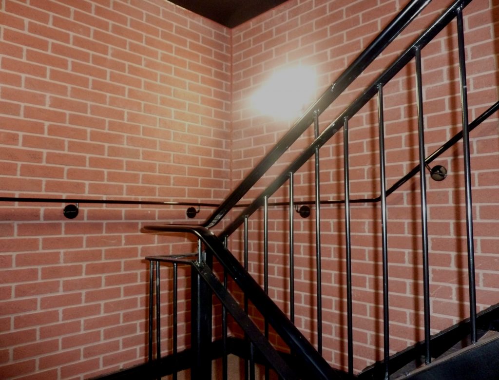 A stairwell with glossy black stairs and banisters, running alongside a GRP brick-effect cladded wall