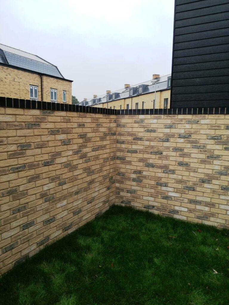 A section of a small cladded property wall surrounding a lawn