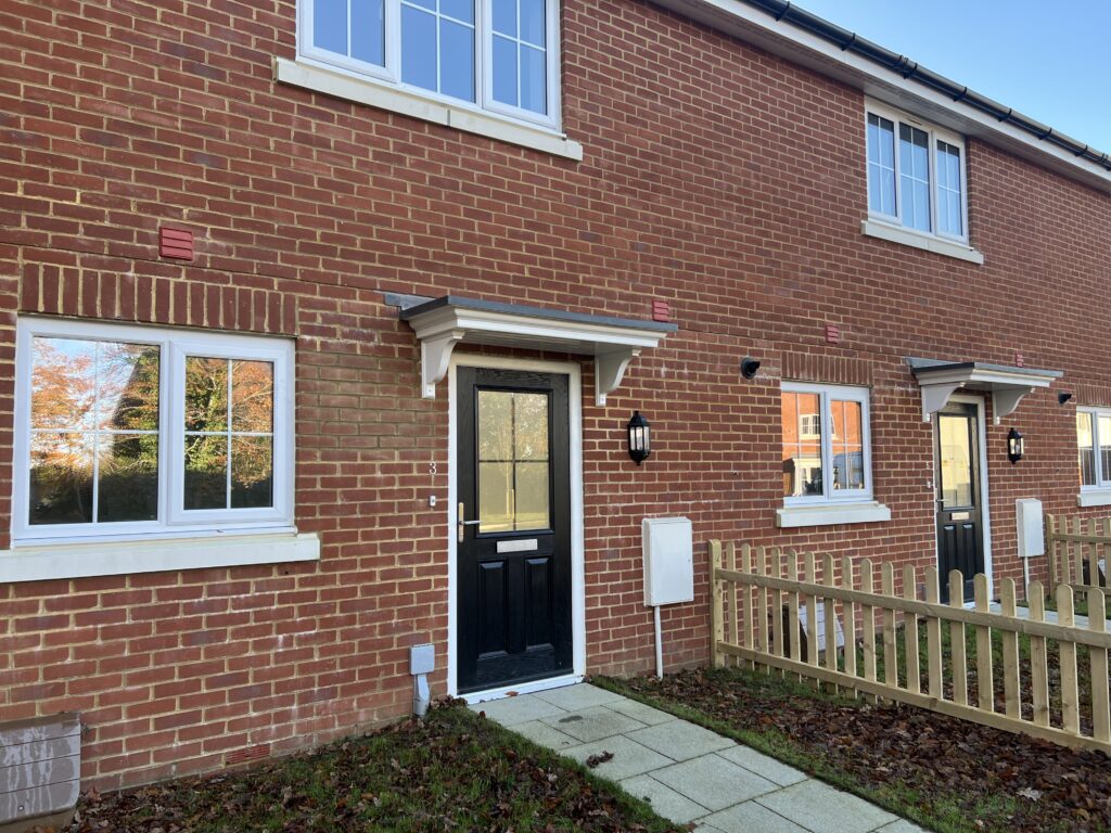 Two new build terraced houses with black front doors and flat GRP canopies above