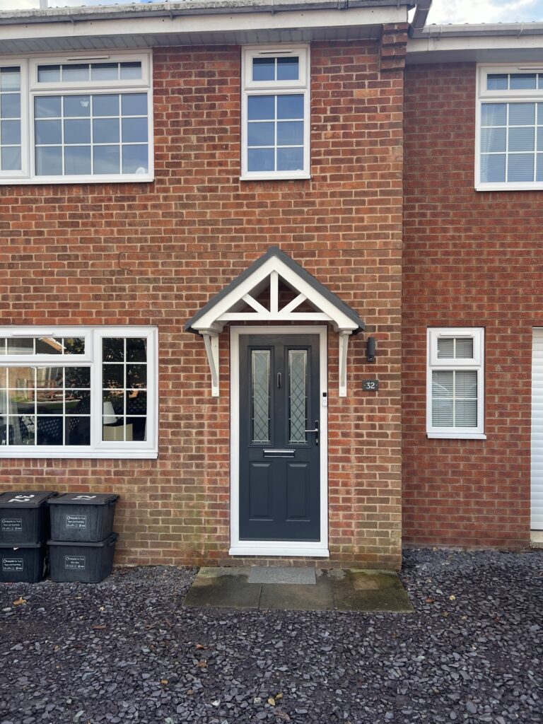 A new build house surrounded by slate, with a white duo pitch GRP canopy with a grey roof above the front door