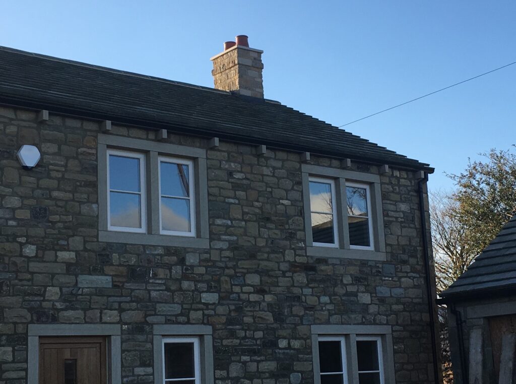 A two flue GRP chimney on the roof of a mixed stone brick house